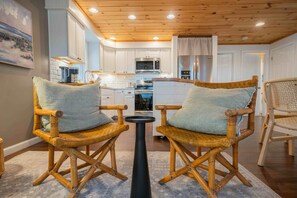 A modern kitchen with white cabinets, a microwave, and a coffee machine. There are two wicker chairs with cushions and a small round table. - Walk to the Beach ~ 2-Bed Kinney Shores Retreat! (Saco)