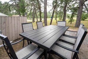 Ulkoilmaruokailualue, jossa on pitkä pöytä ja kuusi tuolia, ja jonka ympärillä on puita.