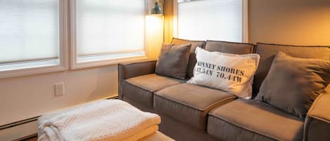 A cozy living room with a sofa, a throw blanket, and a pillow with text.