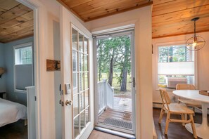 A room with a wooden ceiling, a door leading to an outdoor area with a view of trees, a table with chairs, and a ceiling light fixture. - Walk to the Beach ~ 2-Bed Kinney Shores Retreat! (Saco)