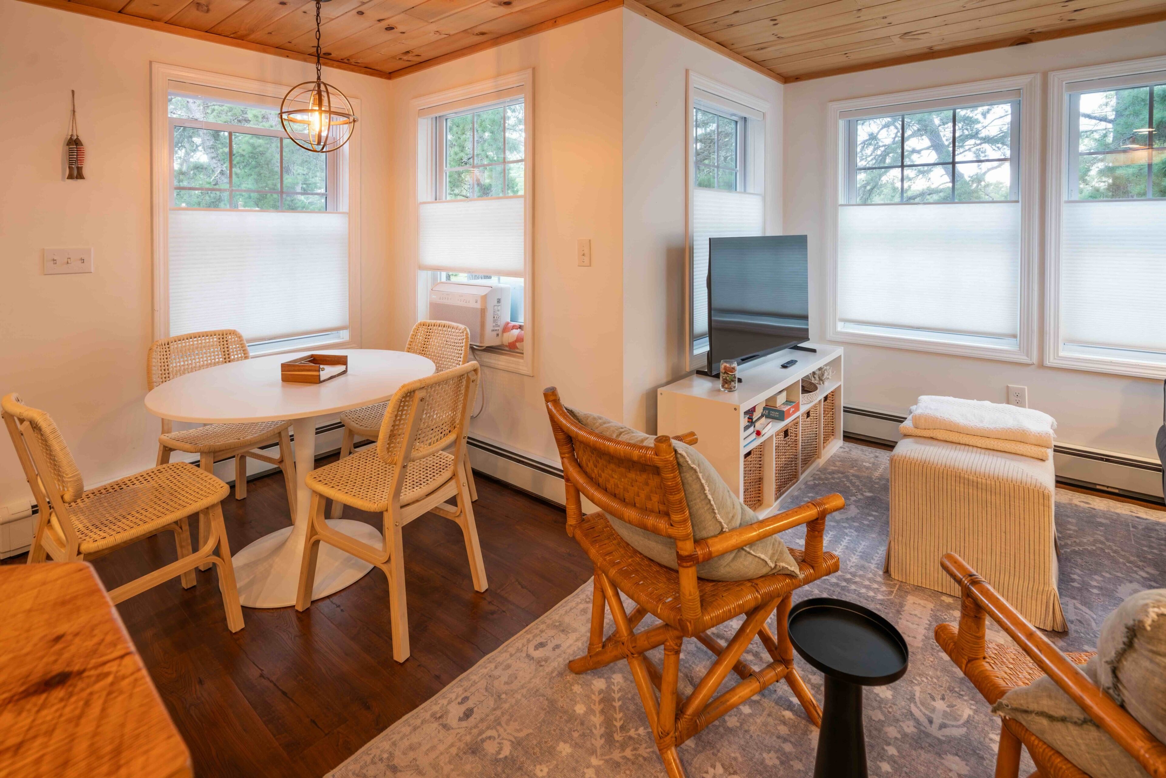 Una habitación acogedora con una mesa redonda para comer, sillas de mimbre, un televisor y una ventana con persianas.