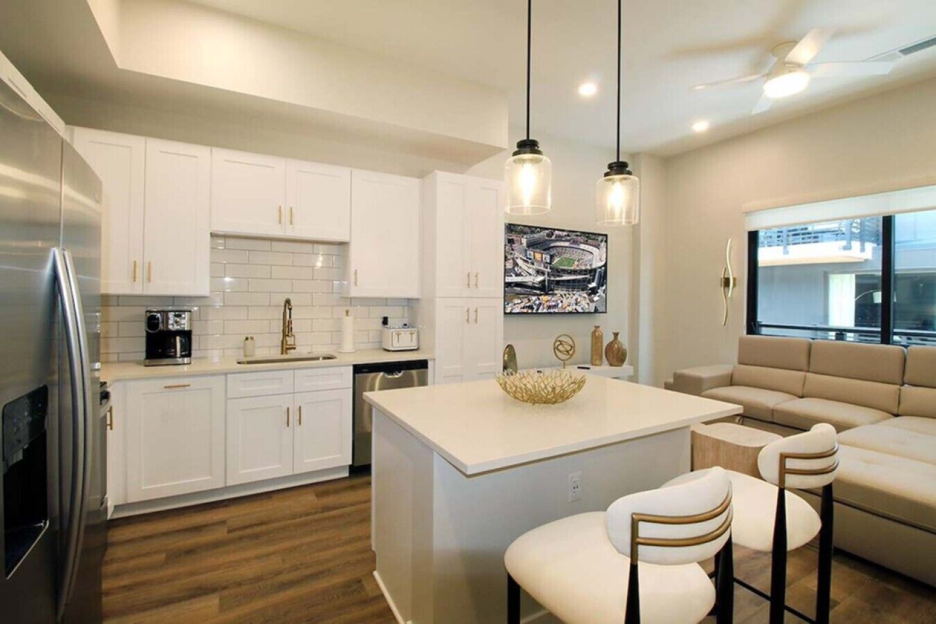 A modern kitchen with white cabinetry, a central island, bar stools, and pendant lighting.