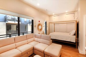 A modern bedroom with a large window, a bed, a sofa, and a decorative wall piece. - City Lights in South Gay | Knoxville (Knoxville)