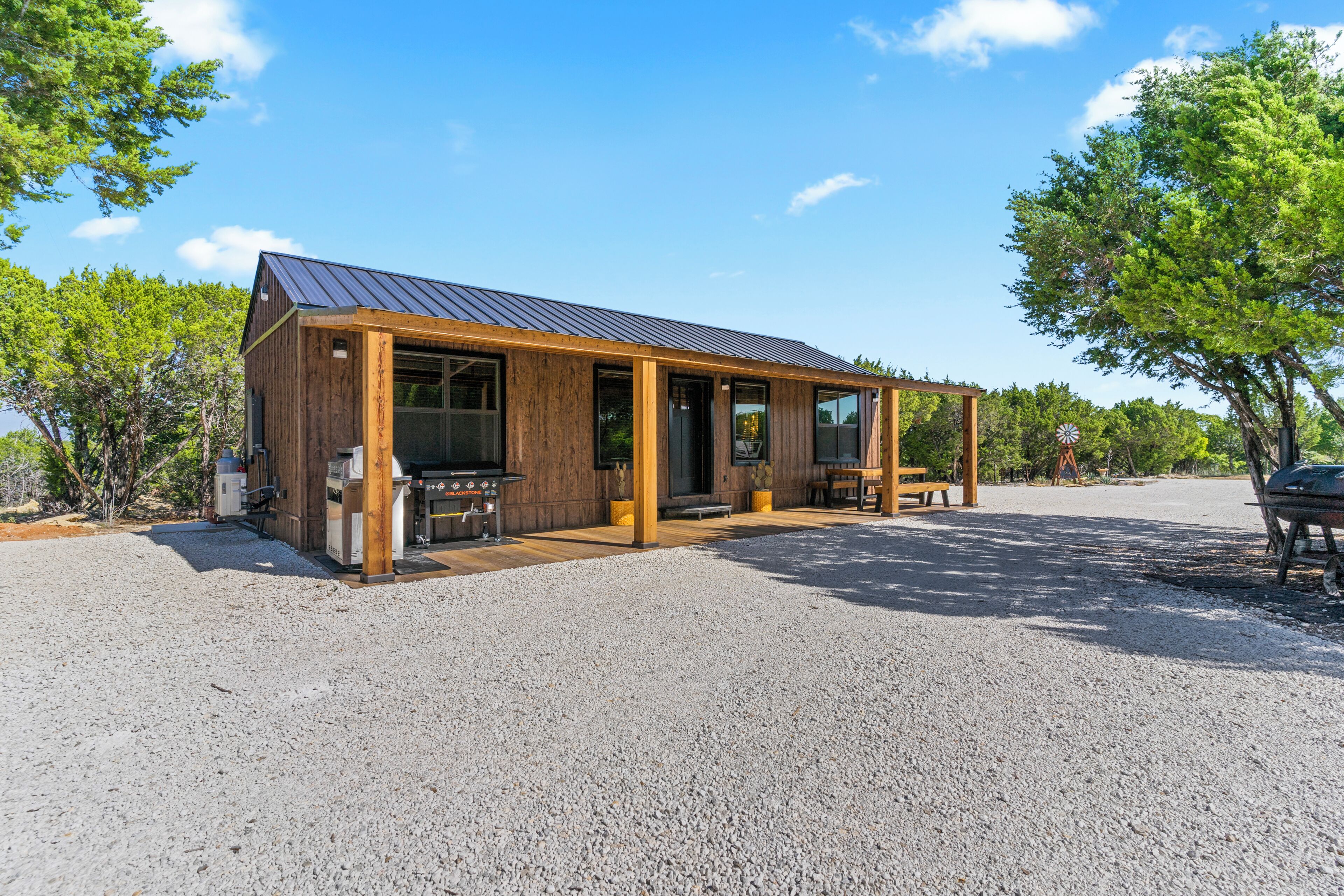 A wooden cabin with a metal roof, a barbecue grill, and a gravel driveway.