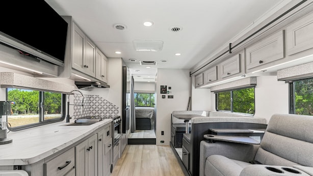 A compact RV interior with a kitchenette, a dining area, and a sleeping berth.