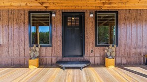 A wooden building with a black door, two windows, and a small porch area with two cactus plants.