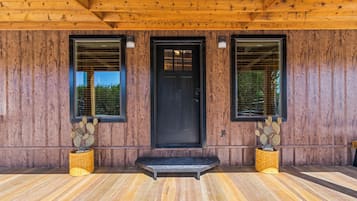 A wooden building with a black door, two windows, and a small porch area with two cactus plants.