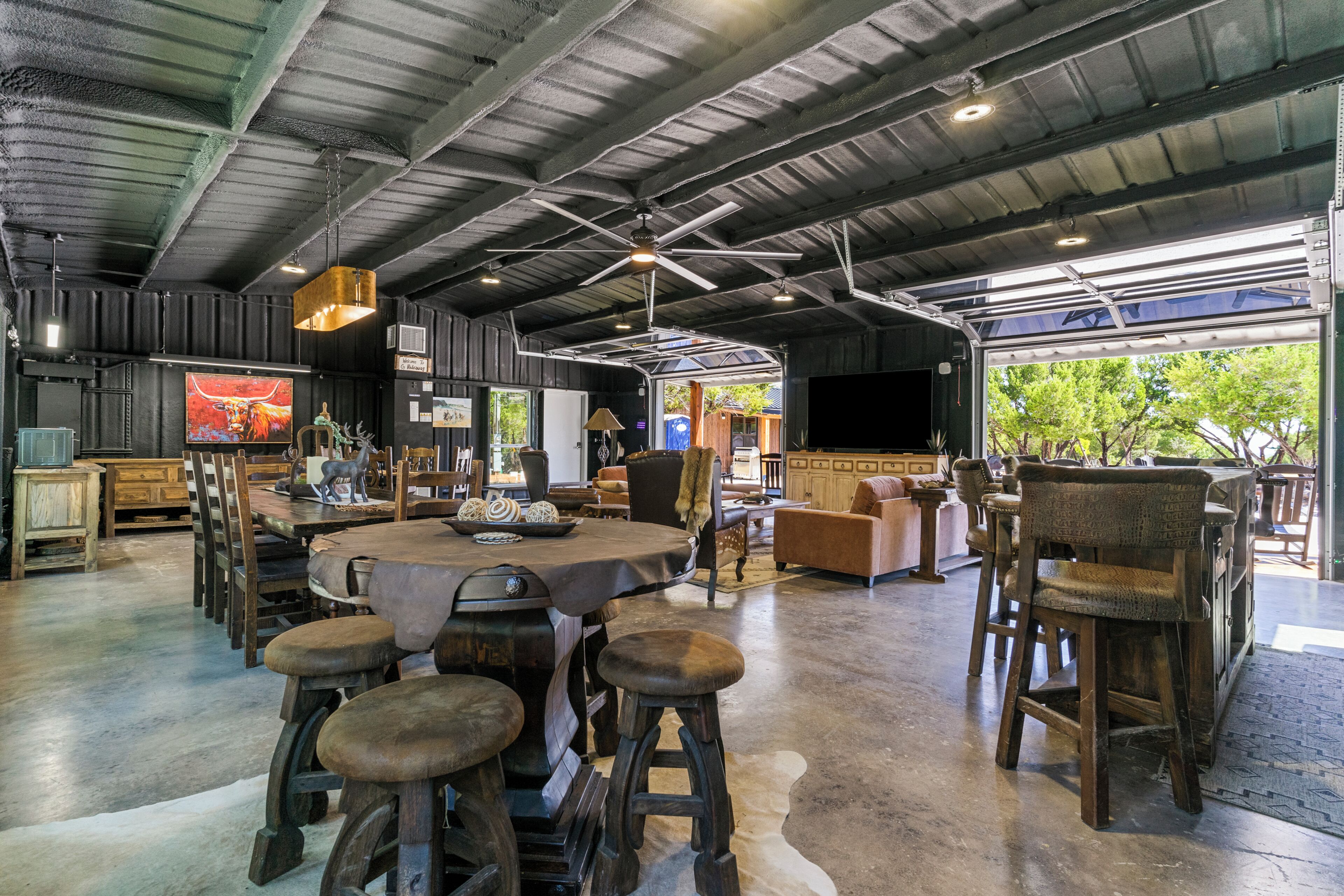 A spacious indoor area with a high ceiling, a central round table surrounded by stools, and a seating area with sofas and chairs.