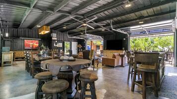 A spacious indoor area with a high ceiling, a central round table surrounded by stools, and a seating area with sofas and chairs.