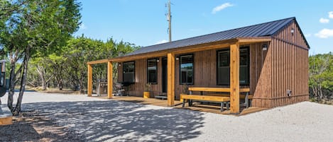 A wooden cabin with a covered patio, a barbecue grill, and a bench.