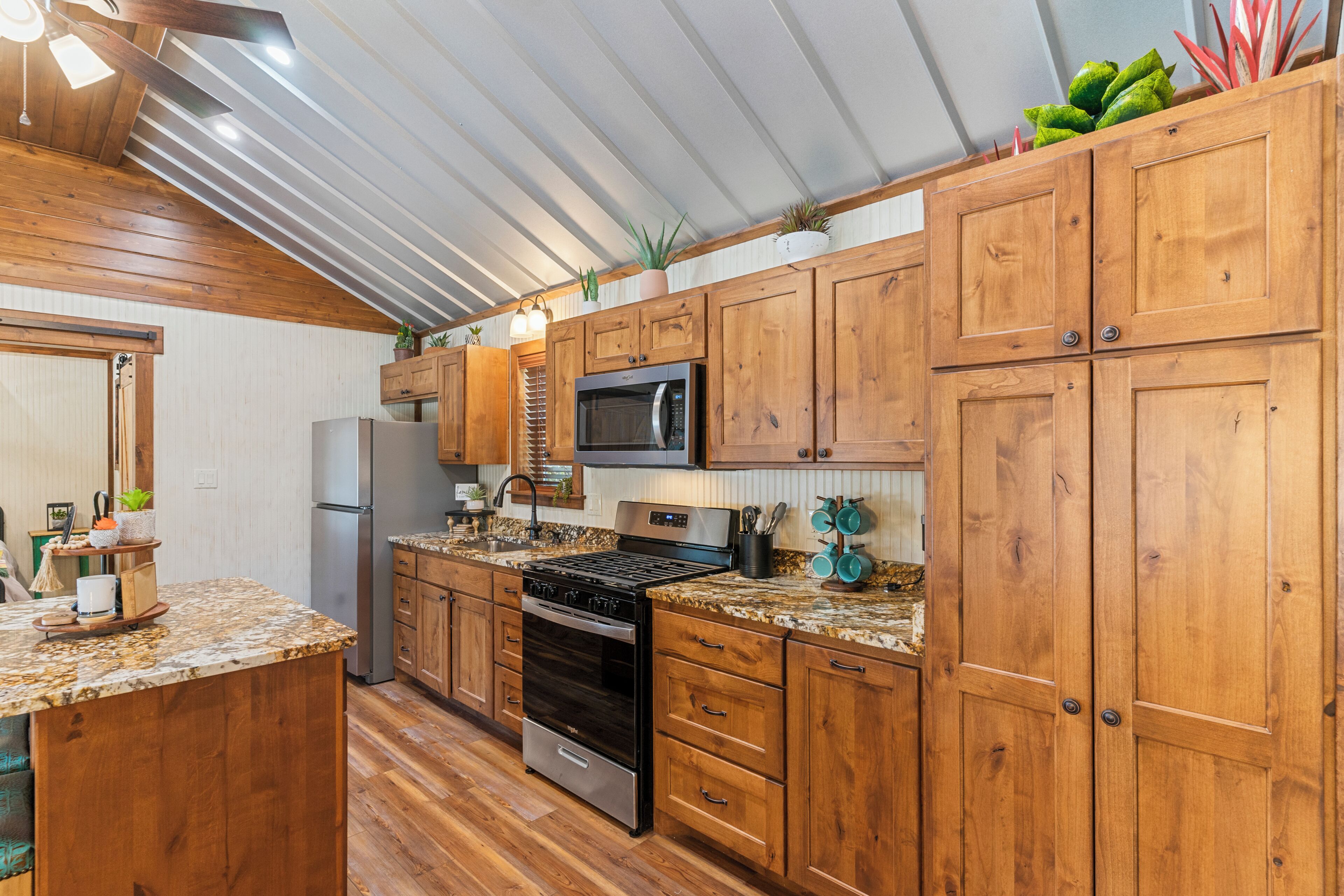 A kitchen with wooden cabinets, a stainless steel refrigerator, a microwave, an oven, and a granite countertop.