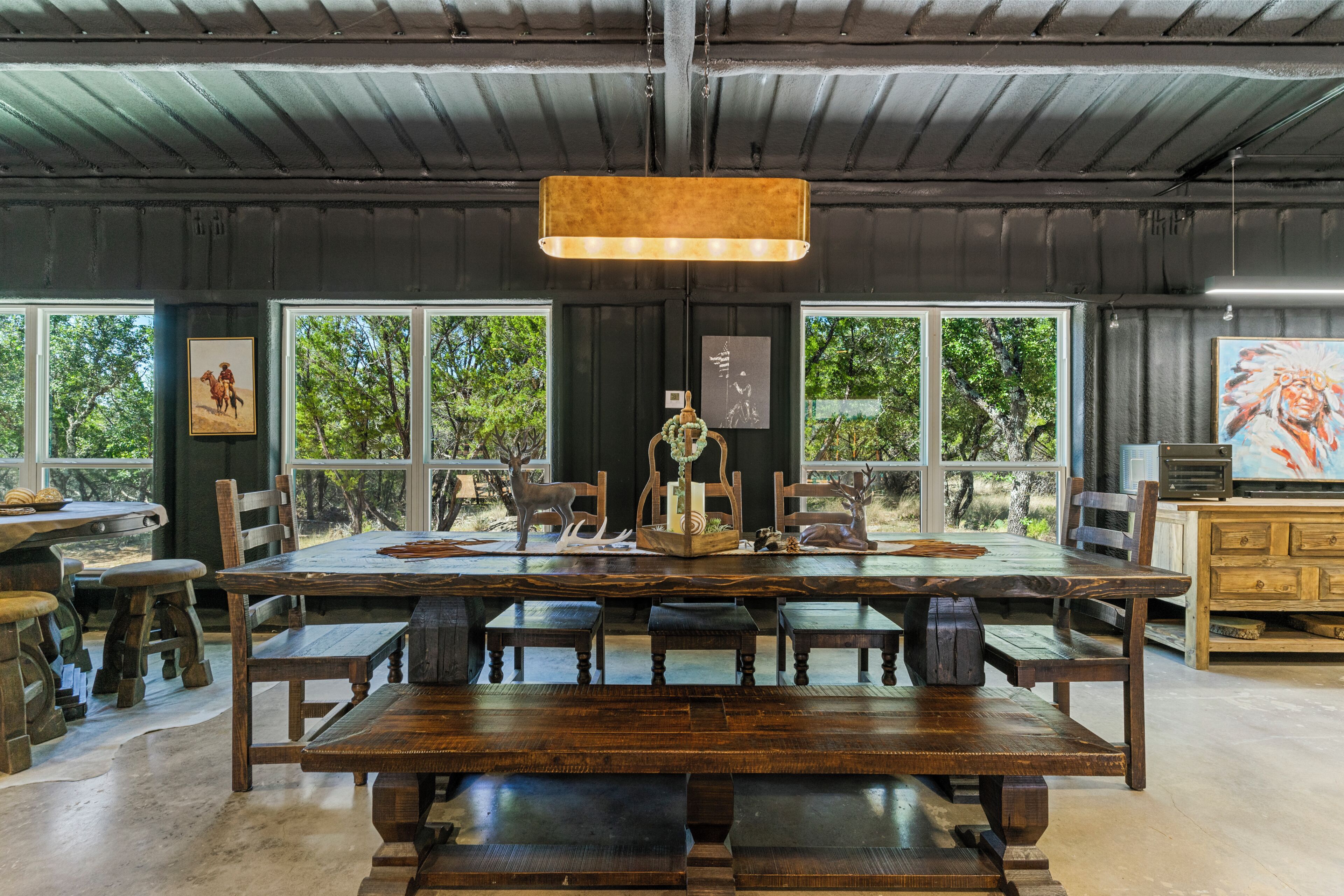 Un coin repas rustique avec une grande table en bois, des bancs et un luminaire suspendu.