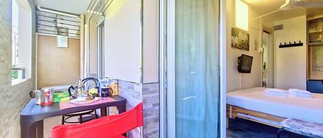 A compact room with a bed, a small table, a chair, and a sliding glass door leading to an outdoor area.
