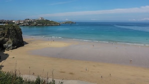 A coastal beach with a clear sky, a sandy shore, and a distant building on a hill. - Higher Tower Road (Newquay)