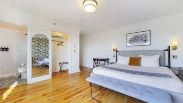 A modern bedroom with a large bed, a desk, and a bathroom visible through an archway.