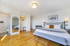 A modern bedroom with a large bed, a desk, and a bathroom visible through an archway. - The Palms at 76 (Miami Beach)