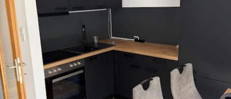 A compact kitchen with dark cabinetry, a built-in oven, and a dining area with a table and two chairs.