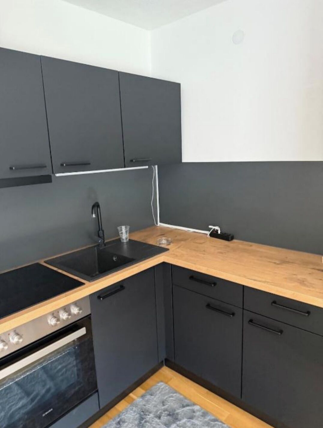A compact kitchen with a black stove, a sink, and dark cabinets.
