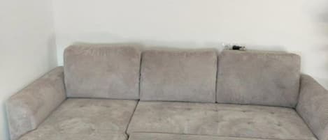 A sectional sofa with a light grey fabric, positioned against a plain wall with a wooden floor.