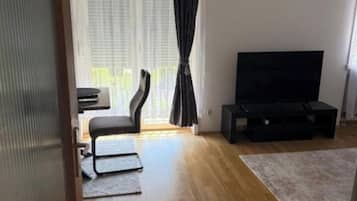 Una sala de estar con televisión de pantalla plana, un sofá, una mesa de centro y un ventanal con cortinas.