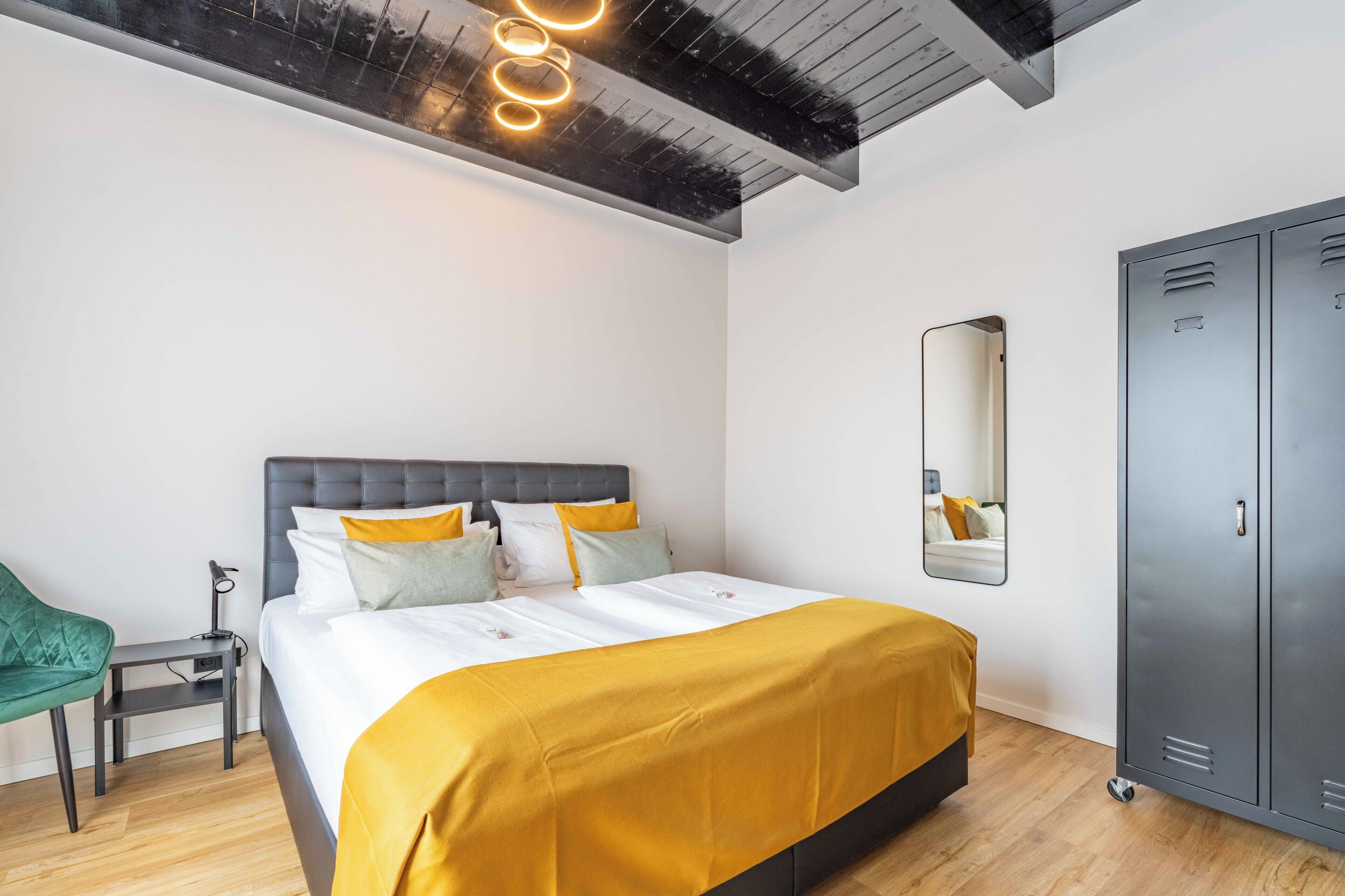 Ein modernes Schlafzimmer mit einem Bett, einem grünen Sessel, einem Spiegel und einer Reihe von Schränken.