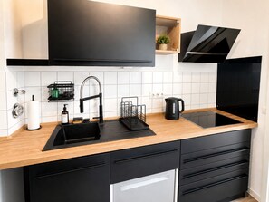 A modern kitchen with a black sink, stainless steel faucet, black cabinets, and a wooden countertop.