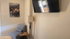 A room with a bed, a patterned chair, a table, a lamp, and a painting on the wall.
