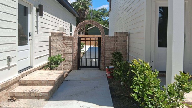 A residential property with a gated entrance, a brick archway, and a small garden area with shrubs.