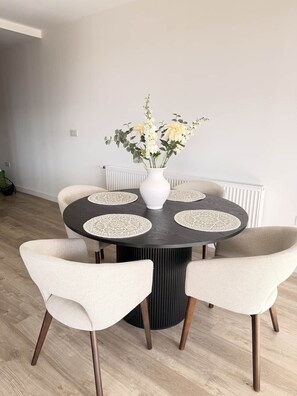 Ein Essbereich mit einem runden Tisch, vier Stühlen, einer Blumenvase und einem Heizkörper im Hintergrund.