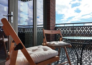 Un balcon avec deux chaises en bois, une table et une vue sur le ciel, visible à travers une porte vitrée.