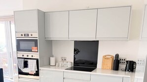 Une cuisine moderne avec des meubles blancs, un four encastré et une plaque de cuisson à induction noire.