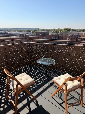 Ein Balkon mit zwei Holzstühlen und einem Glastisch, mit Blick auf die Skyline.