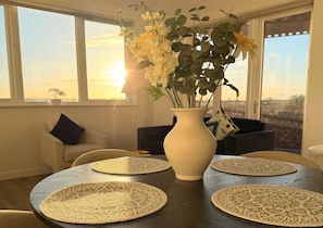 Ein Essbereich mit einem runden Tisch, einer Blumenvase und Blick auf die Stadt durch große Fenster.