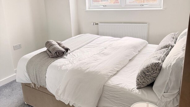 Une chambre à coucher avec un lit, un radiateur, une fenêtre et une lampe sur une table de chevet.