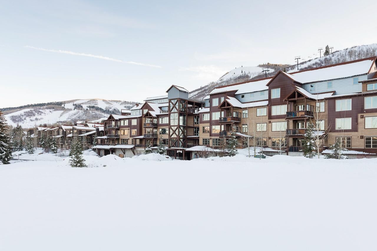 Une station de ski enneigée, avec des bâtiments à plusieurs étages, des pistes de ski en arrière-plan et un paysage montagneux.