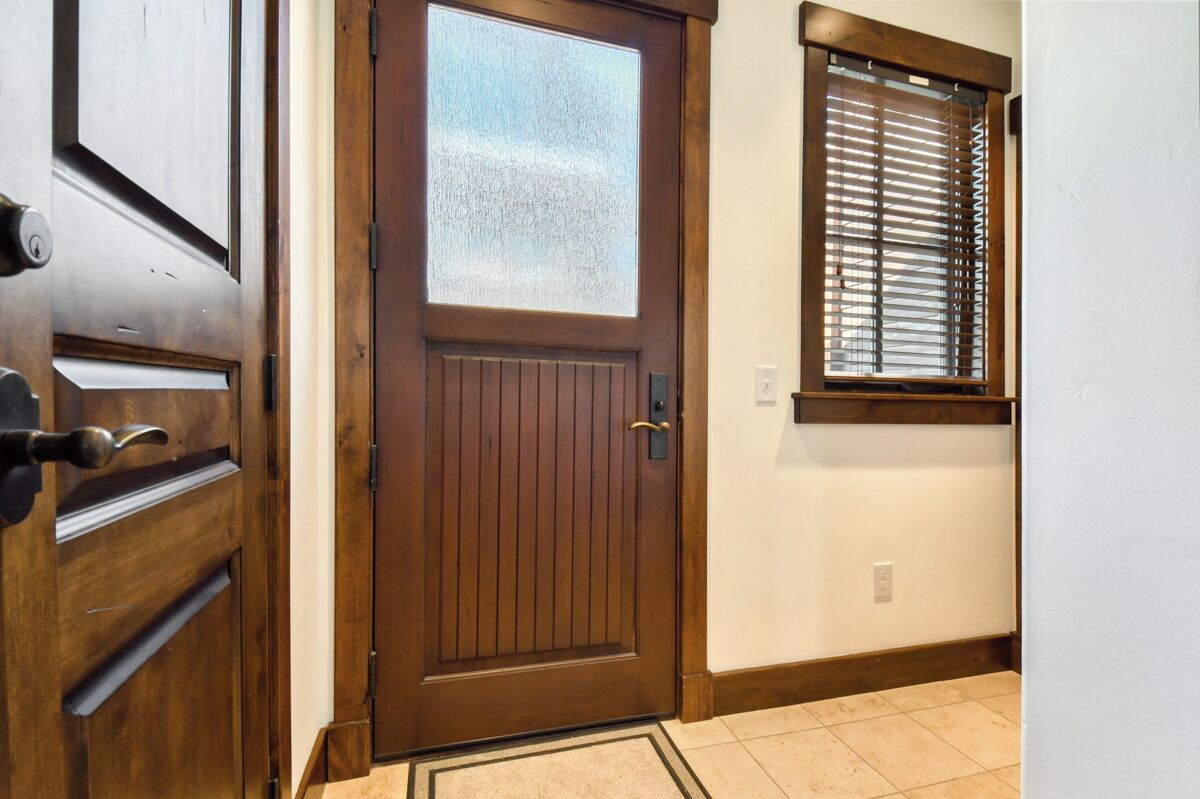 Una puerta de madera con un panel de vidrio, una ventana con persianas y un piso de baldosas.