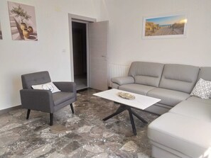 A living room with a grey sofa, a small armchair, a coffee table, and a painting of a beach scene. - Abruzzo Hills Villa – Near the Sea, Villages & Mountains (Treciminiere)