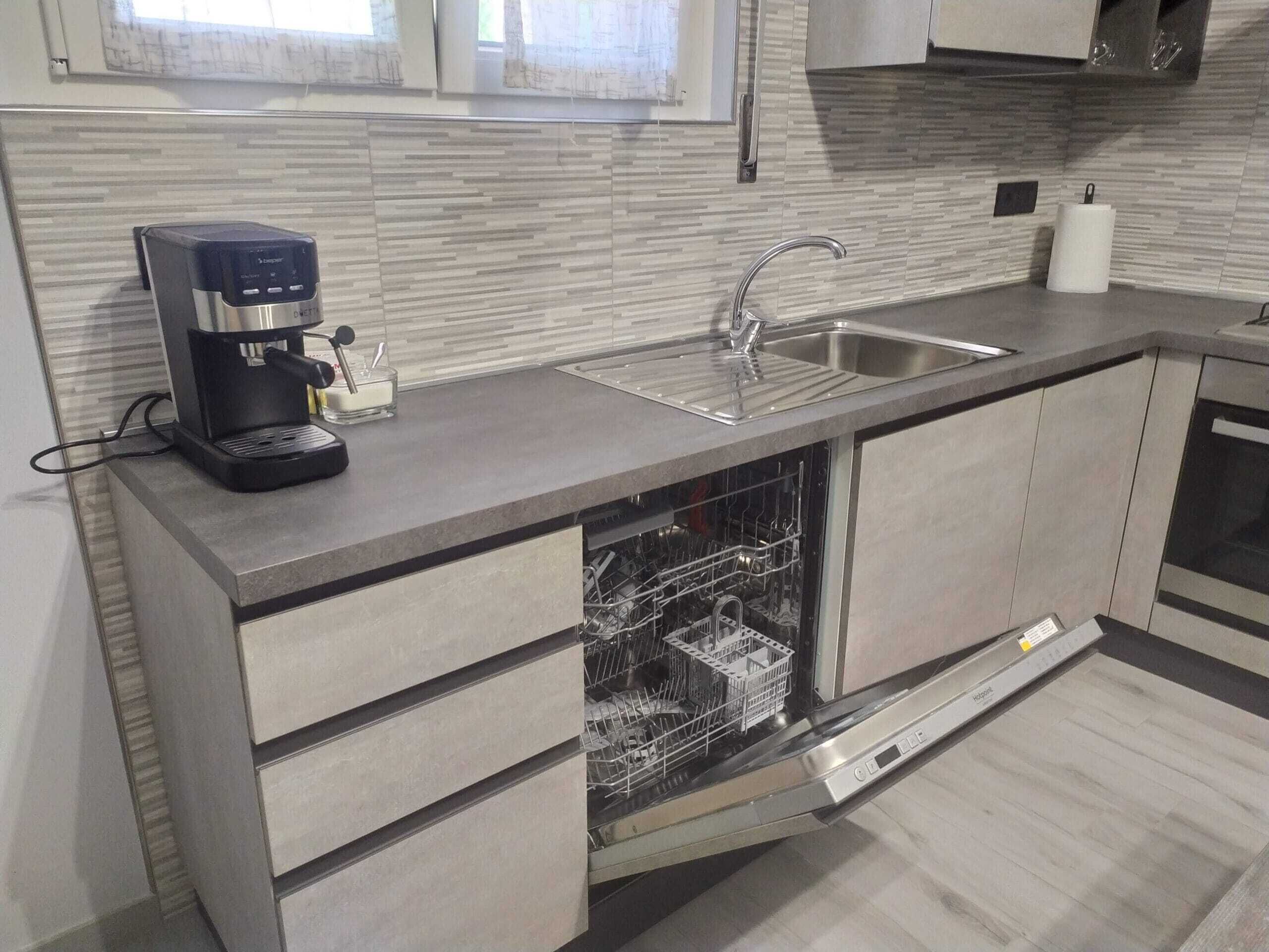 A modern kitchen with a built-in dishwasher, a coffee maker, and a stainless steel sink.