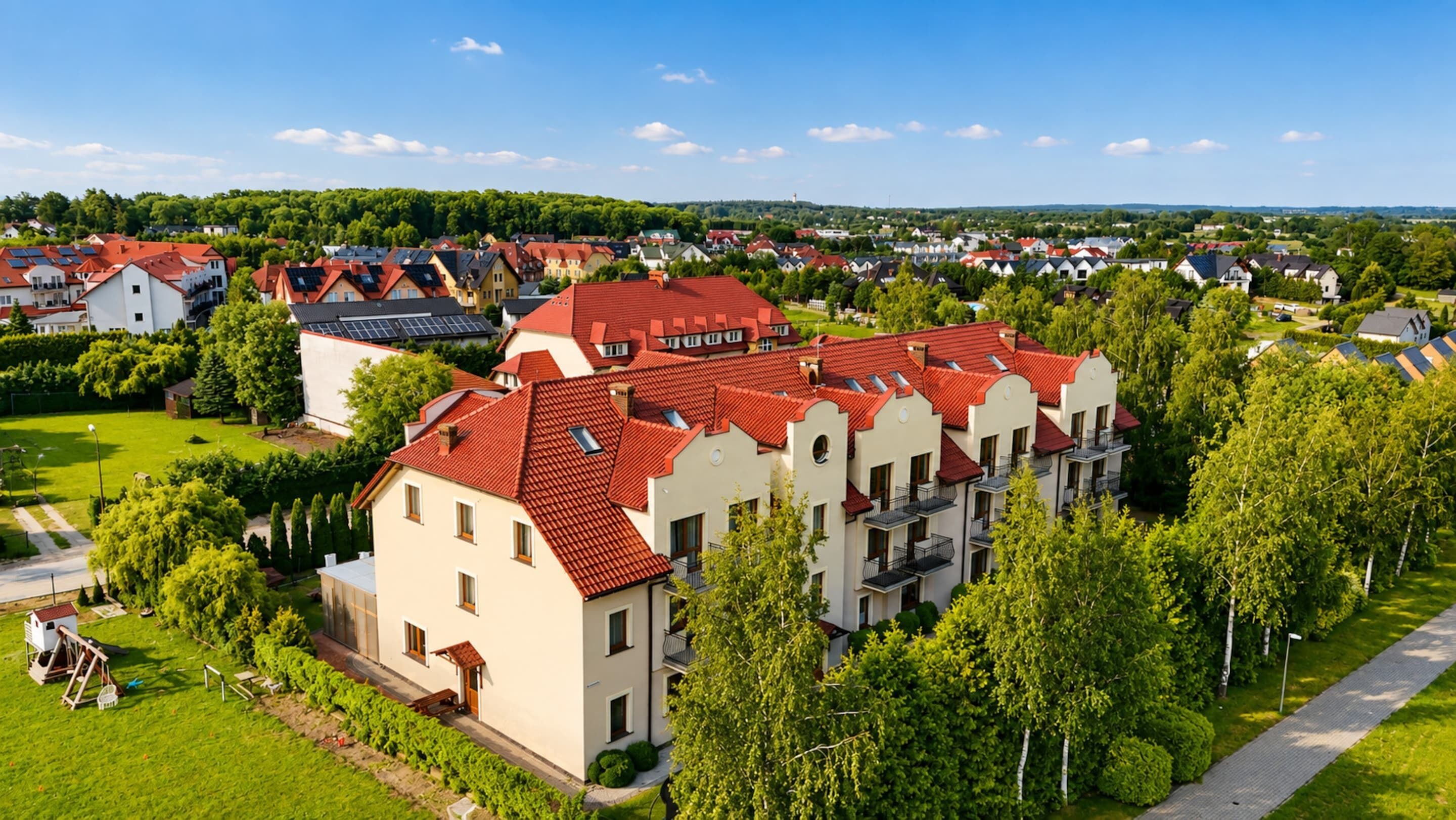 A residential area with multiple houses, some with red roofs, surrounded by greenery and a clear sky.