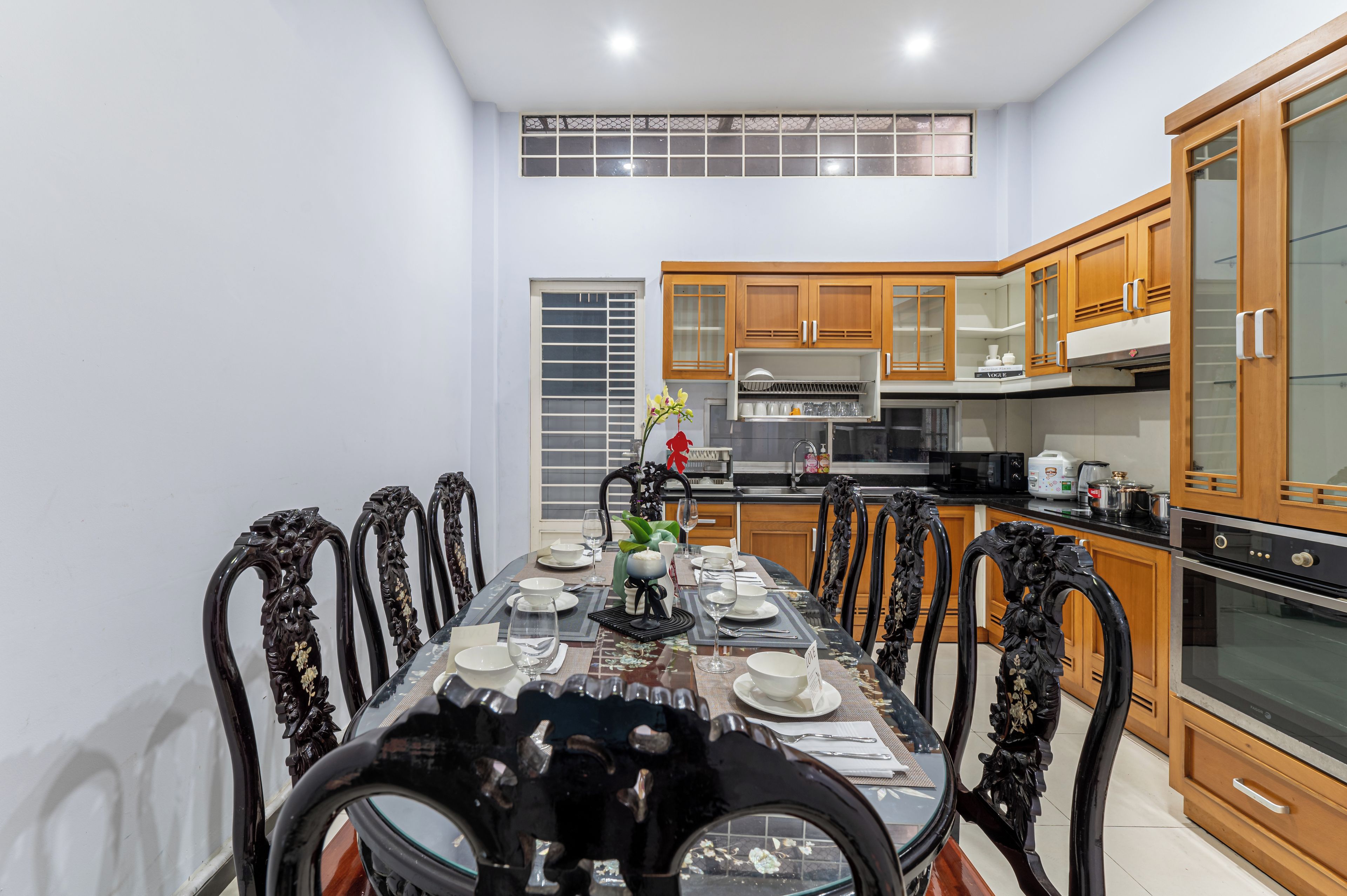 A dining area with a table set for four, surrounded by ornate chairs, in a kitchen with wooden cabinets and modern appliances.