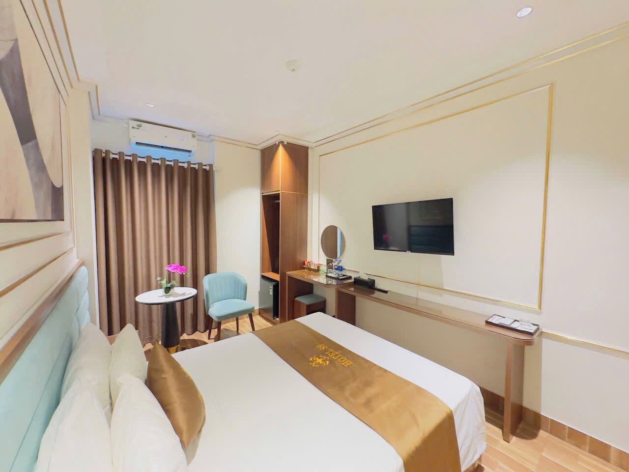 Hotelkamer met een bed, bureau, stoel, televisie en een klein tafeltje met een bloem.