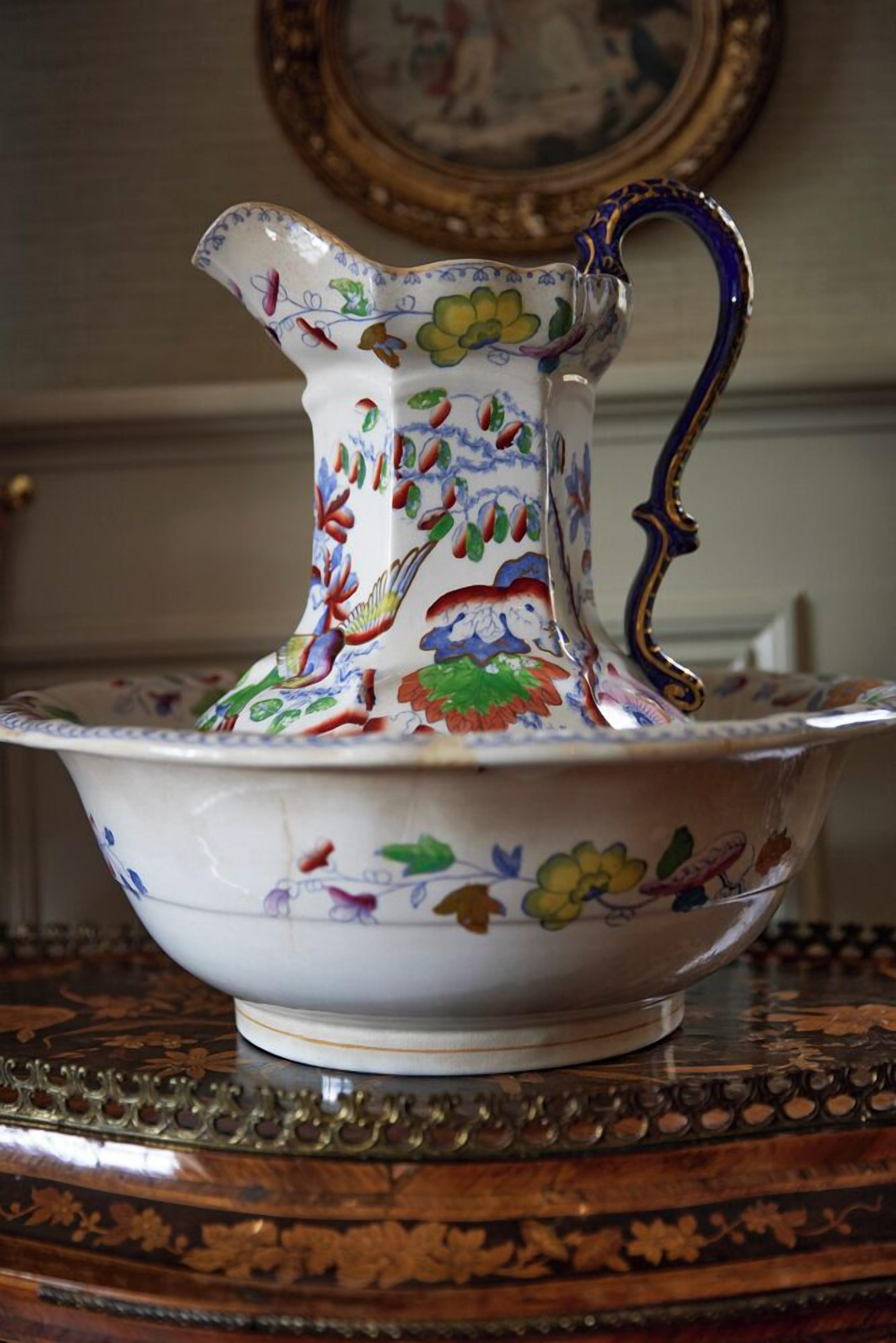 A decorative ceramic pitcher and bowl with floral patterns, placed on an ornate table.