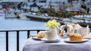 A table with a tea set and pastries, overlooking a waterfront with buildings and greenery. - The Secret Garden (Kinsale)