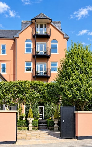 A multi-story residential building with a balcony on each floor, a gated entrance, and a well-maintained garden. - The Secret Garden (Kinsale)