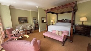 A hotel room with a four-poster bed, a sitting area with a sofa and armchairs, a desk, and a dresser. - The Secret Garden (Kinsale)