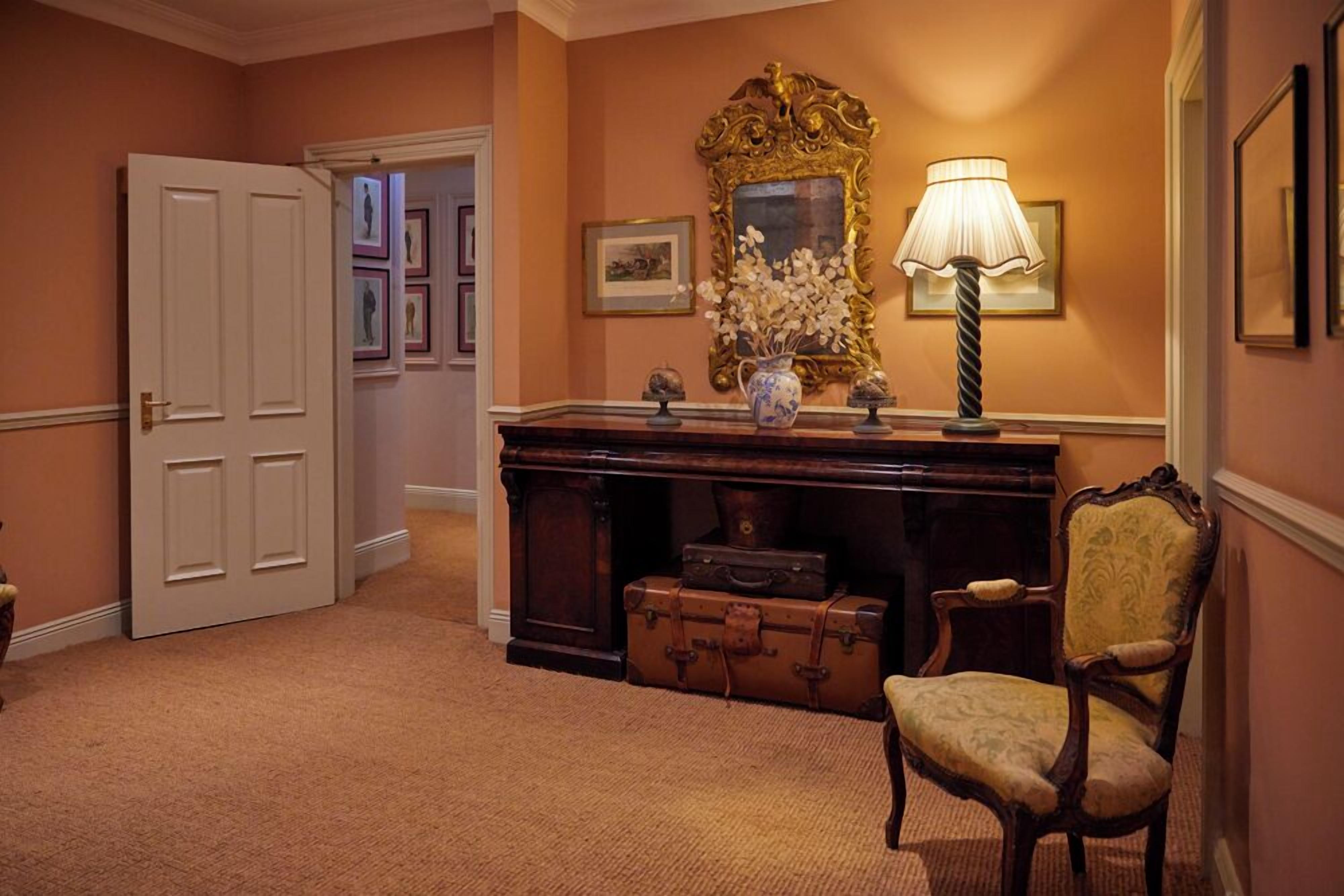 A hallway with a wooden desk, a lamp, a chair, and a door.