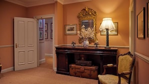A hallway with a wooden desk, a chair, a lamp, a mirror, and a door. - The Secret Garden (Kinsale)
