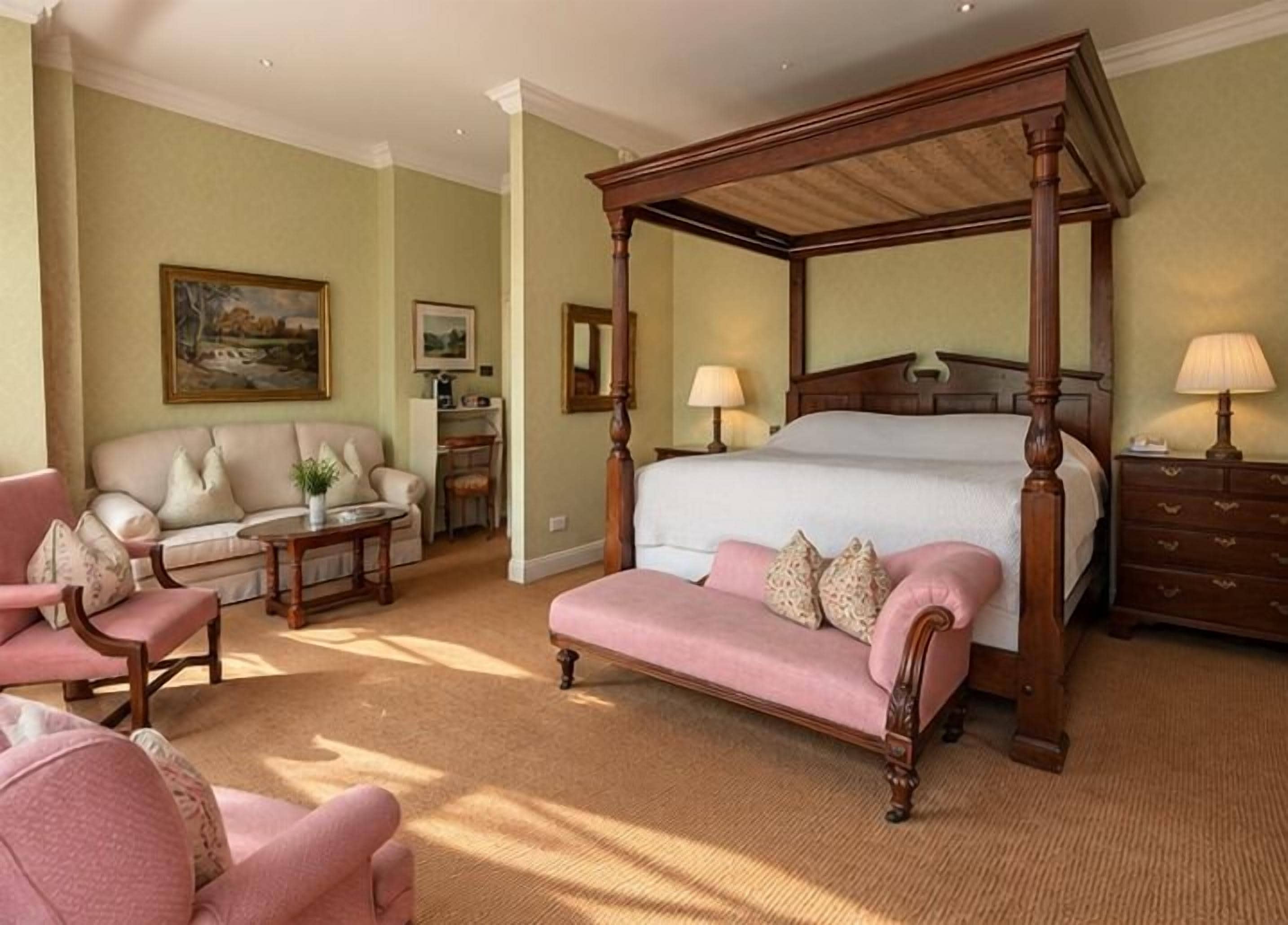 A bedroom with a four-poster bed, a sofa, a chair, and a desk.
