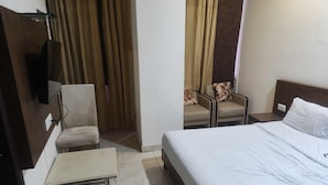 A hotel room with a bed, a small table, a chair, a television, and curtains. - Deluxe Hotel Elegant Palace (New Delhi)