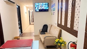 A hotel lobby with a reception desk, a sofa, a television displaying multiple screens, and a fire extinguisher. - Deluxe Hotel Elegant Palace (New Delhi)
